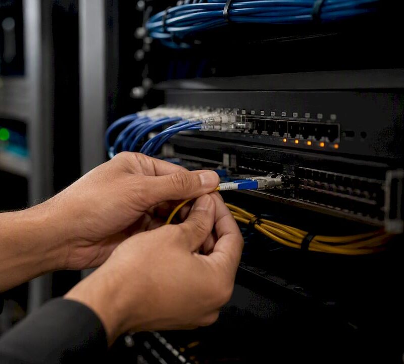 Hands connecting fiber optic cable in server room